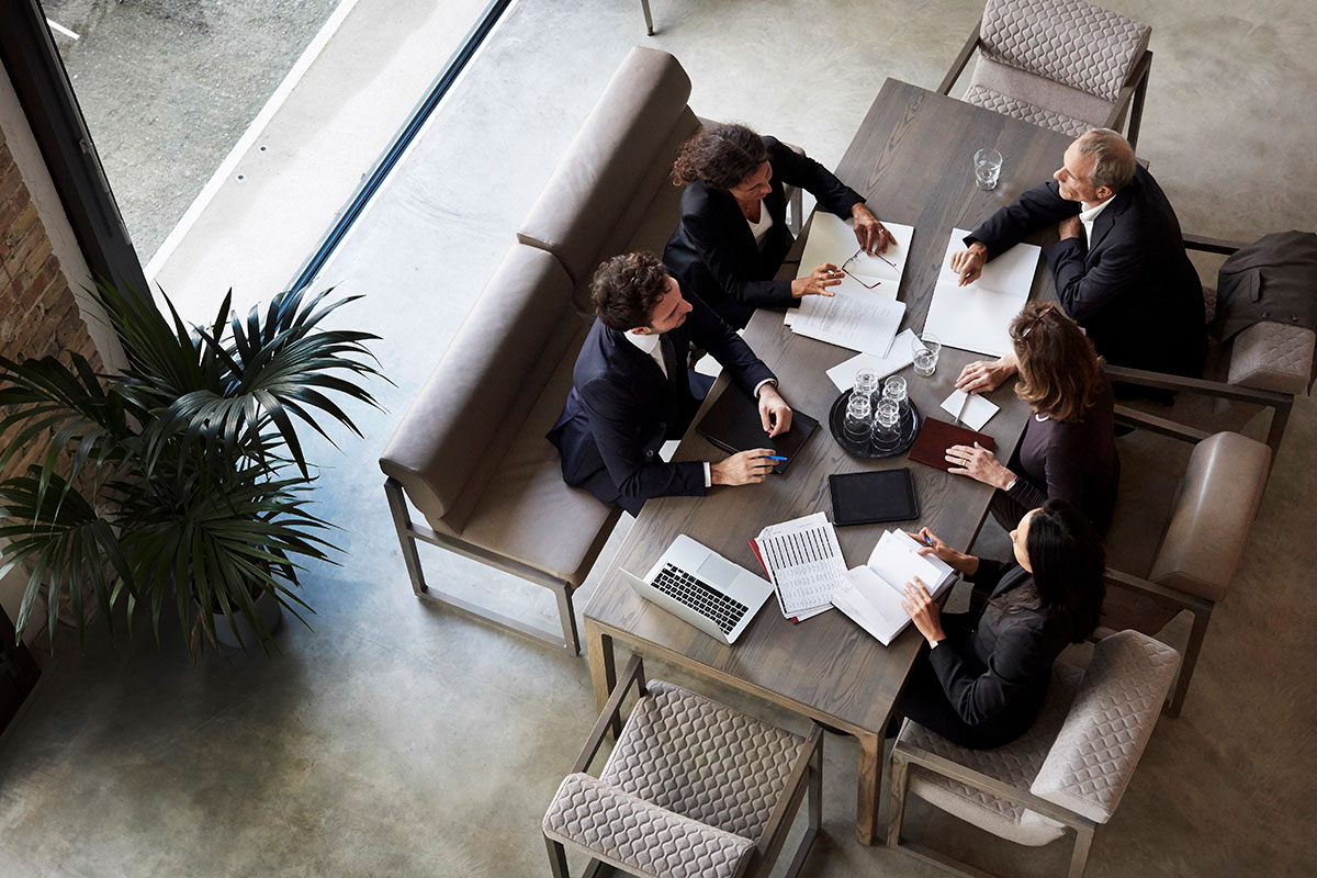 An overhead view above five business professionals having discussion at a common table.