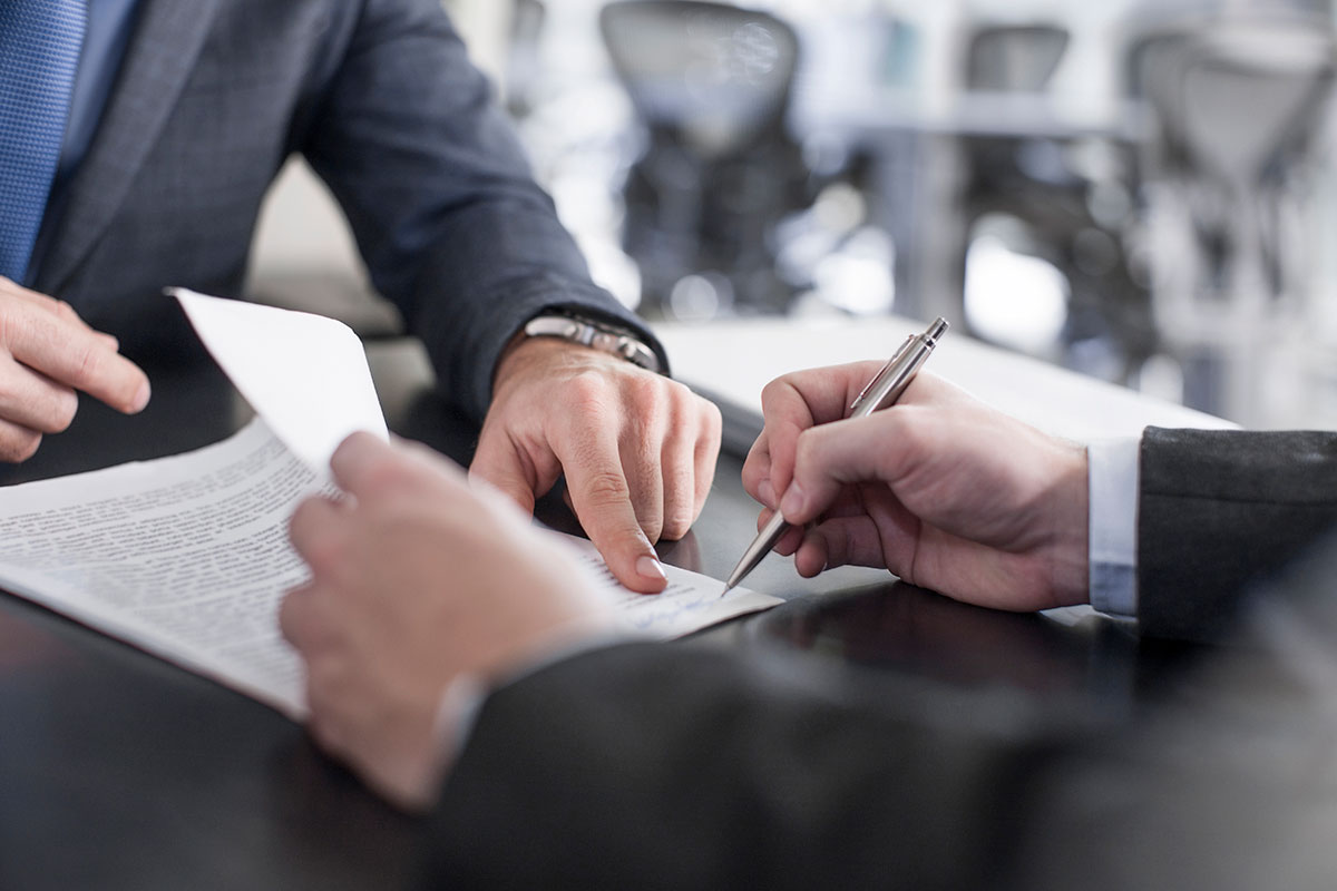 Closeup of a desk where a general liability insurance professional points out where a client should sign a policy.